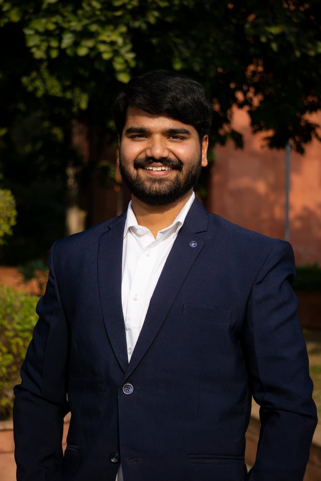 Adarsh Dwivedi in a navy blazer, standing outdoors in the evening.