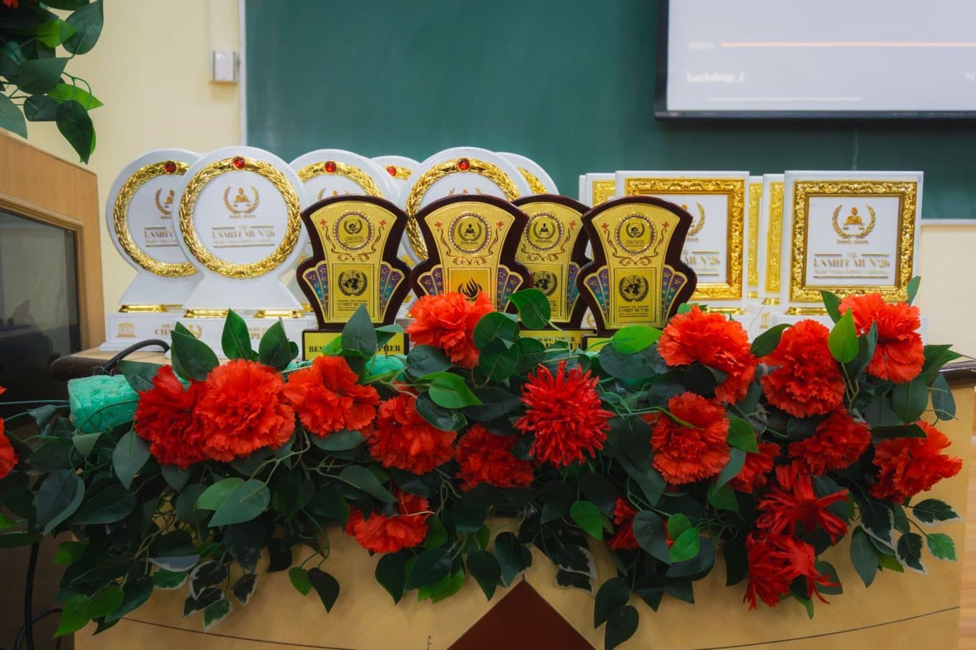 The LNMIIT MUN'26 trophies and certificates laid out behind a row of red flowers.